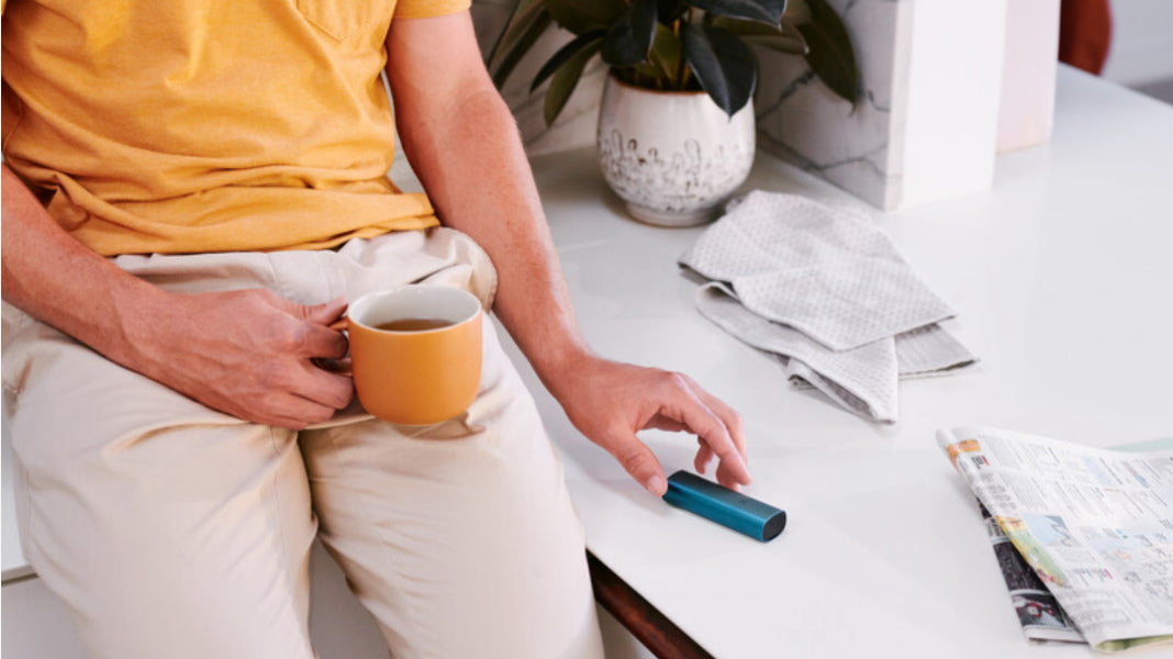 person holding a cup of coffee and reaching for their PAX device