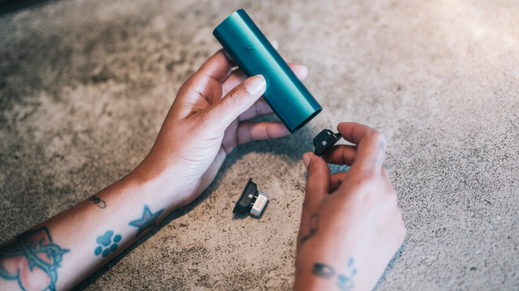 Tattooed hands cleaning a blue PAX Pod