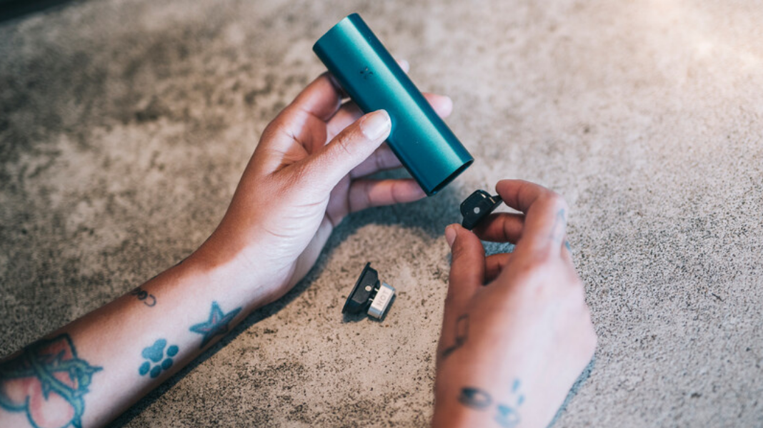 Tattooed hands cleaning a blue PAX vape